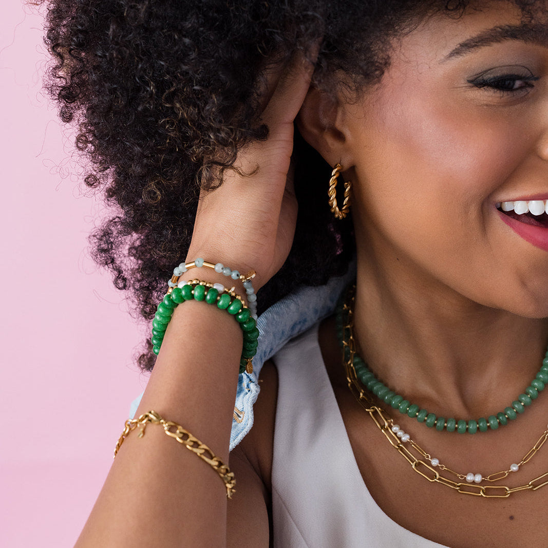 Woman wearing multiple necklaces and bracelets against a pink background